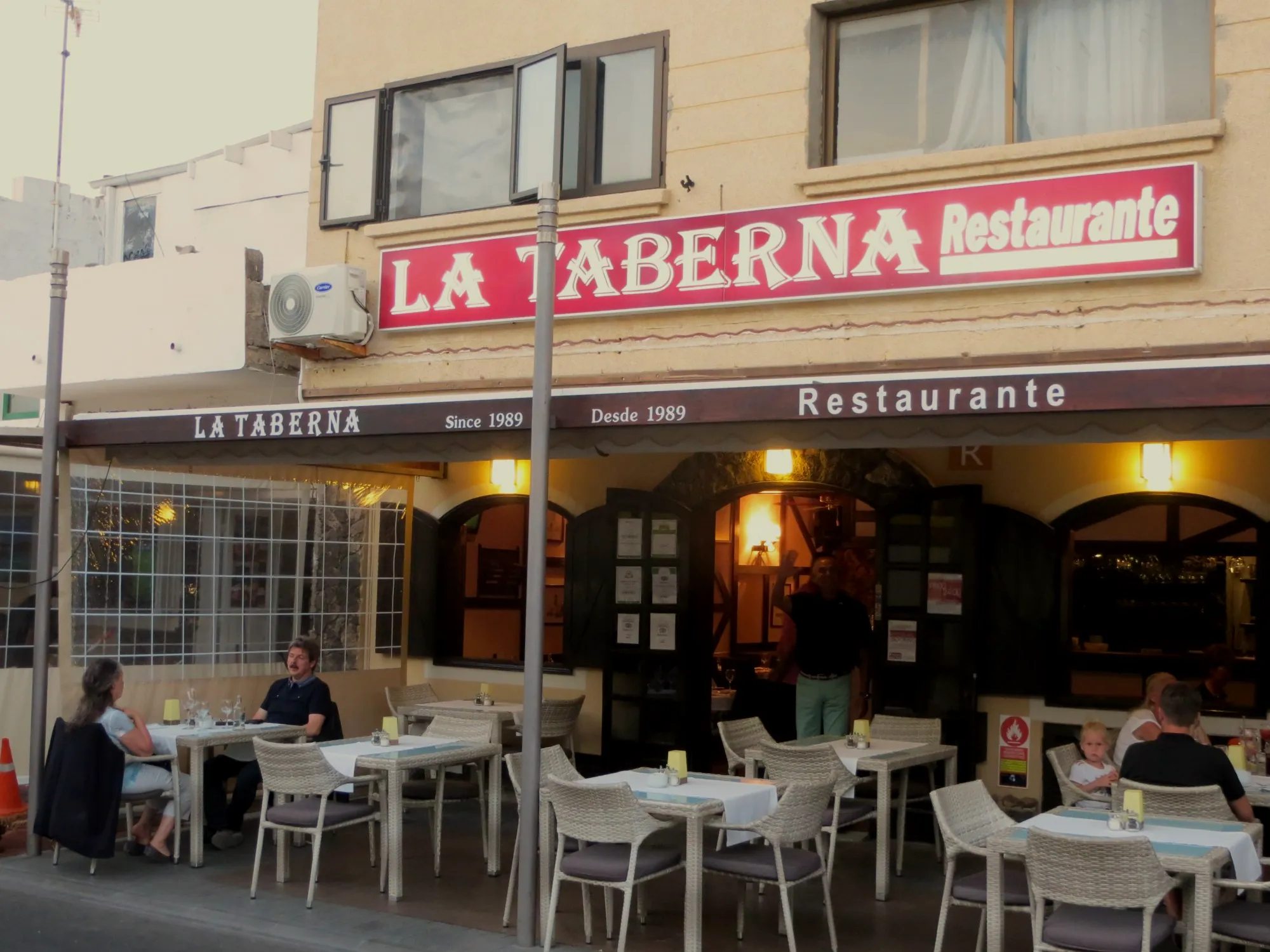 Fachada de La Taberna en la calle Hernán Cortés al atardecer, con el letrero rojo y la terraza