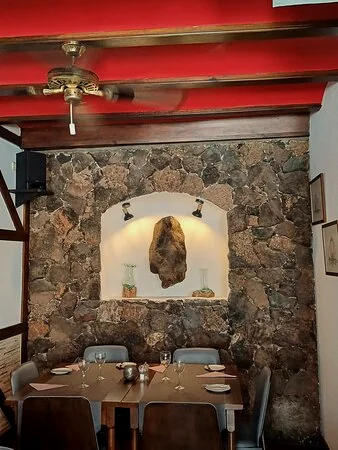 Comedor interior con pared de piedra volcánica y vigas rojas